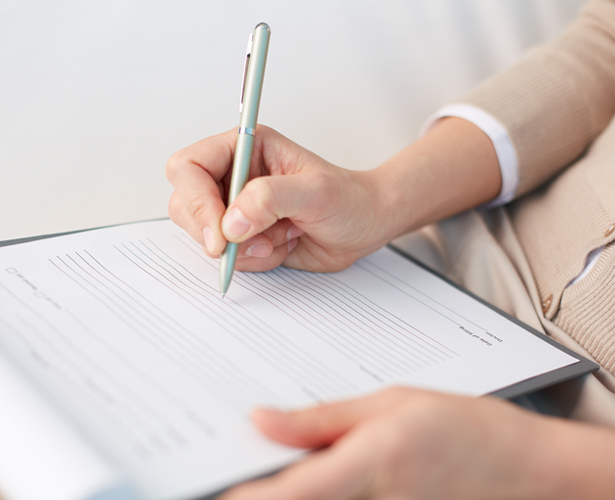 Person writing on a lined form or document with a pen at a desk.